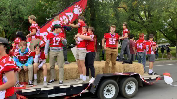 Un grupo de estudiantes en el Ashland School District está en un remolque sosteniendo banderas rojas en un parque.