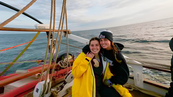 Dos estudiantes de la Ashley Hall School están en la cubierta de un velero con mar abierto y cielo nublado de fondo.