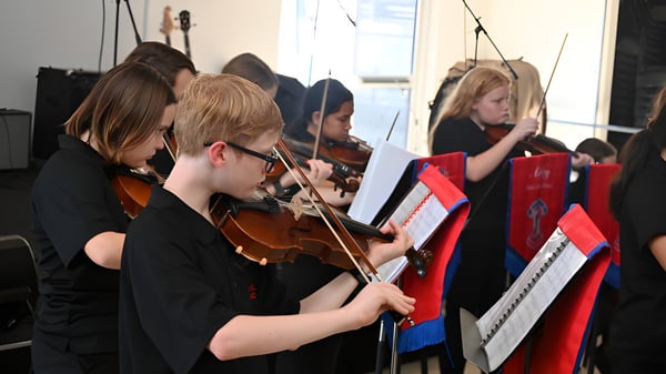Un grupo de jóvenes músicos de la Aspley State High School toca concentradamente instrumentos de cuerda durante una actuación.