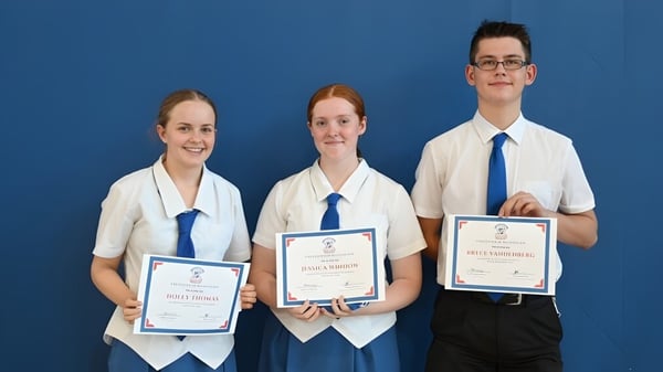 Tres estudiantes de la Aspley State High School sostienen juntos sus certificados frente a un fondo azul.