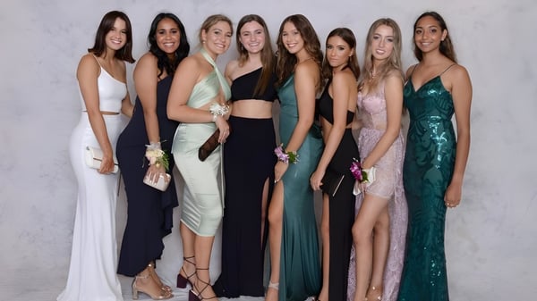 Un grupo de estudiantes de la Assumption Grammar School posan en vestidos de noche frente a un fondo blanco.
