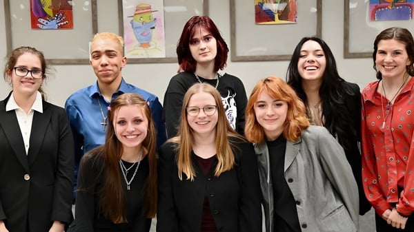 Un grupo de alumnas está juntas en un interior en el campus de la Athens Christian School frente a un arte mural colorido.