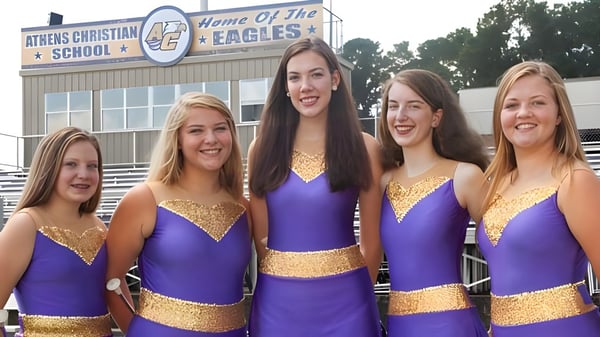 Cinco alumnas en uniformes de animadoras están frente a un edificio de la Athens Christian School.