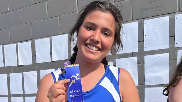Una joven sonríe frente a una pared de concreto gris en el campus de la Athens District High School.