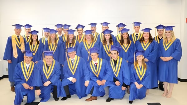 Un grupo de graduados de la Athens District High School está en togas azules y amarillas frente a un fondo blanco.