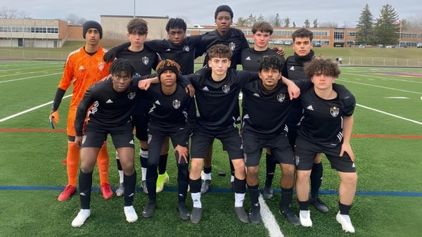 Un grupo de alumnas y alumnos del Athlete Institute posan en el campo de fútbol frente a un edificio escolar.
