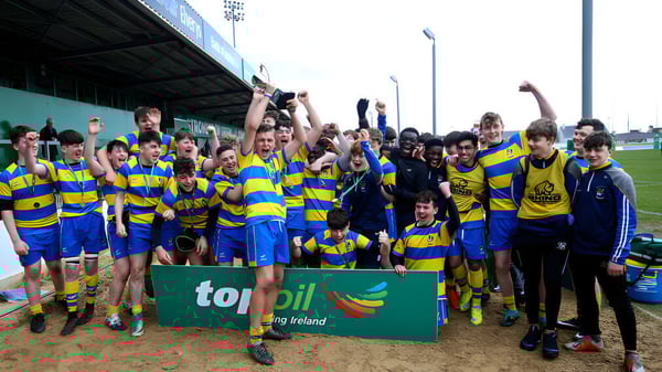 Estudiantes del Athlone Community College celebran juntos en un campo deportivo y sostienen una bandera en alto.