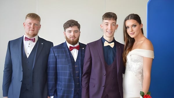 Cuatro personas posan con ropa formal frente a un fondo azul en el campus del Athy College.