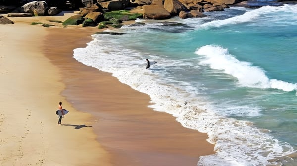 Dos personas caminan por la playa con acantilados y olas cerca del Atwell College.