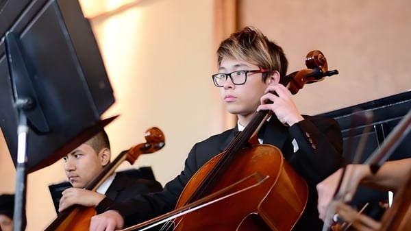 Un estudiante de la Auburn Adventist Academy toca el cello en el escenario con otros músicos al fondo.