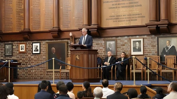 Un hombre está en el podio y habla ante una gran audiencia en el suntuoso salón de la Auckland Grammar School.