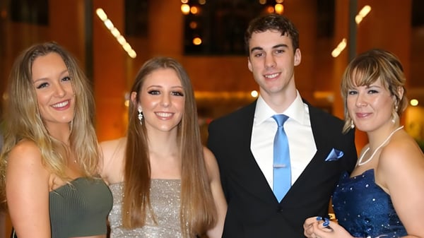 Cuatro personas, dos mujeres y dos hombres, posan juntos frente a un fondo decorativo en el campus de la Australian Science and Mathematics School.
