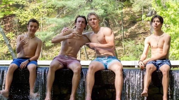 Cuatro jóvenes están sentados sin camiseta en un muro con vista a un paisaje boscoso en el terreno de la Avon Old Farms School.