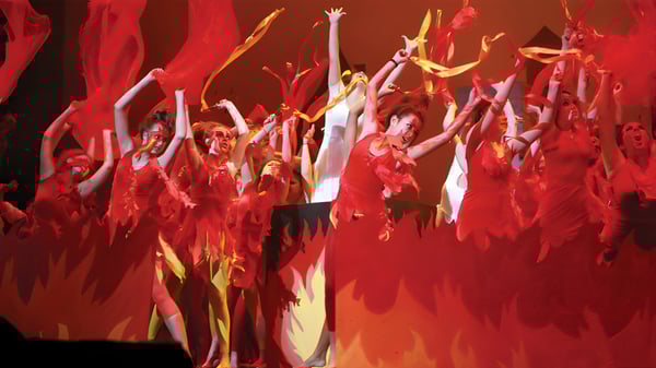 Un grupo de bailarinas y bailarines del Avondale College realiza una dinámica actuación con trajes rojos y amarillos.