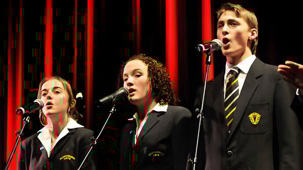 Tres estudiantes del Awatapu College actúan en el escenario frente a cortinas rojas y cantan en micrófonos.