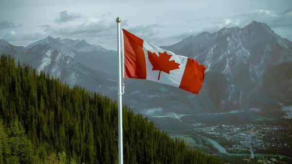 Una gran bandera canadiense ondea frente a montañas cubiertas de nieve y un valle boscoso en el terreno de la A.Y. Jackson Secondary School.