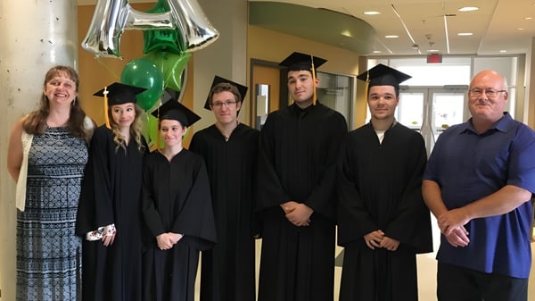 Un grupo de estudiantes de la A.Y. Jackson Secondary School está en túnicas y birretes en el pasillo con globos y decoración.