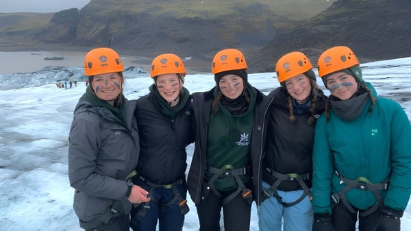 Un grupo de estudiantes de la Badminton School está en paisajes montañosos nevados usando cascos de protección naranjas.