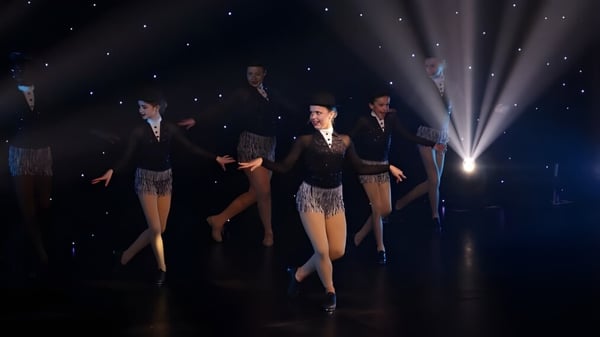 Estudiantes de la Badminton School realizan un baile en un escenario con fondo estrellado vestidos de manera formal.