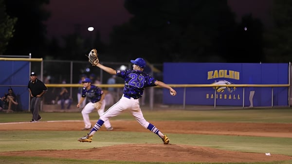 Un jugador de béisbol de Bakersfield Christian lanza la pelota en el campo por la noche bajo las luces.