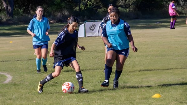 Jugadoras de fútbol de la Balga Senior High School entrenan en un campo de césped durante un evento deportivo.