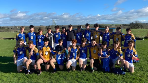 Un grupo de estudiantes de la Balla Secondary School está juntos en uniformes deportivos en un campo de césped con cielo nublado.