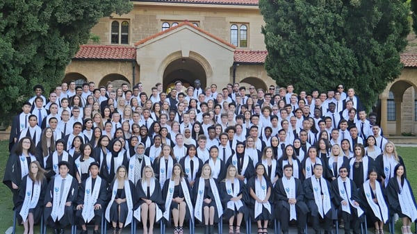 Un grupo de estudiantes en ropa de graduación está de pie frente a un edificio histórico en el campus del Ballajura Community College.