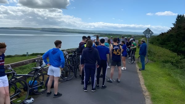 Un grupo de alumnas y alumnos de la Ballingarry Presentation School están en un sendero con vistas a un lago y colinas boscosas.