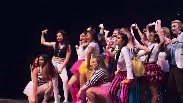 Un grupo de jóvenes estudiantes del Ballybay Community College realiza una actuación en el escenario frente a un fondo oscuro.