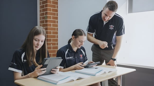 Tres estudiantes utilizan dispositivos electrónicos en una mesa en el campus del Ballybay Community College.