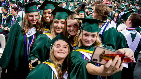 Un grupo de graduados de la Balmoral State High School en togas de graduación verdes se toma un selfie juntos.