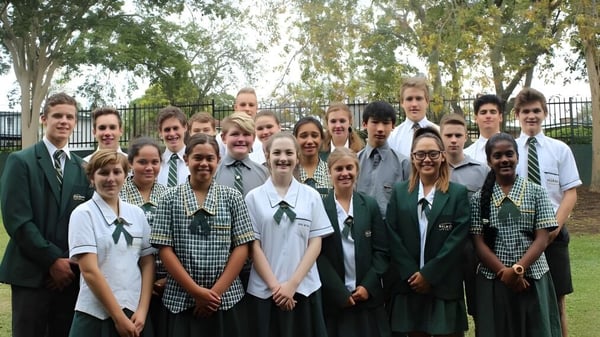 Un grupo de estudiantes de la Balmoral State High School está afuera frente a árboles y una cerca.