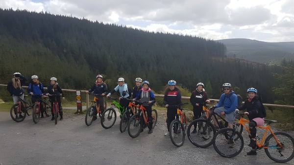 Un grupo de estudiantes en bicicleta está en un camino del bosque en el terreno del Banagher College bajo un cielo nublado.