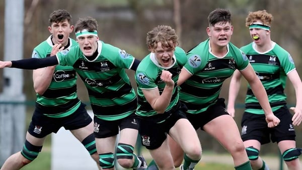 Alumnos de la Bandon Grammar School juegan juntos al rugby en un campo cubierto de hierba con árboles al fondo.