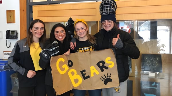 Cuatro estudiantes están de pie frente a un edificio de la Banff Community High School y sostienen un cartel que dice 'Go Bears'.