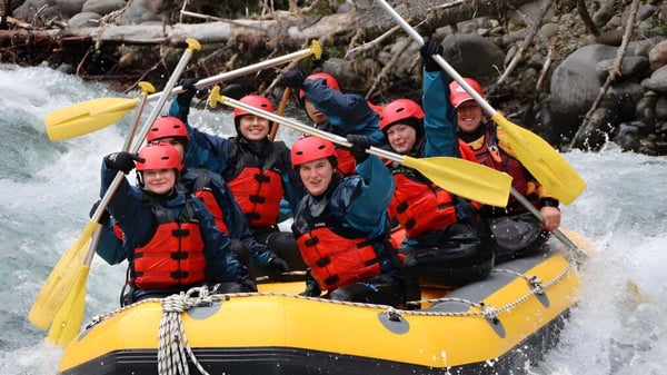 Alumnos de la Barnard Castle School haciendo rafting en un río de aguas bravas en un terreno rocoso.