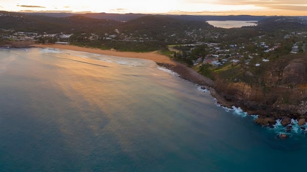 Toma aérea de una ciudad costera con colinas verdes y mar turquesa cerca de Barrenjoey High School.
