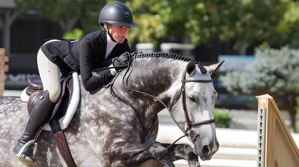 Una estudiante de la Battle Abbey School monta un caballo gris al aire libre frente a árboles y edificios.