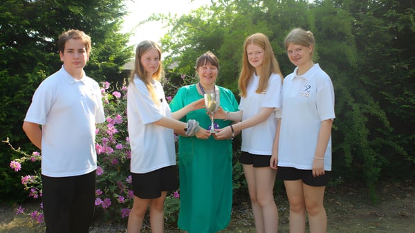 Un grupo de cinco estudiantes está de pie en un área verde al aire libre en el campus del Baxter College.