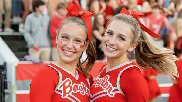 Dos animadoras sonrientes en uniformes rojos en el campus de la Baylor School frente a una multitud.