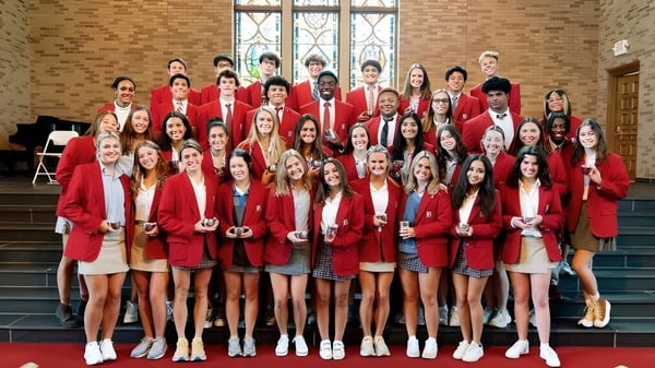 Un grupo de estudiantes de la Baylor School está en togas rojas en la escalera frente a un edificio con vitrales.