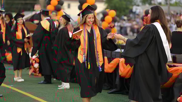 Un grupo de graduados y graduadas en togas negras en la ceremonia de graduación de la Bayridge Secondary School en un prado.