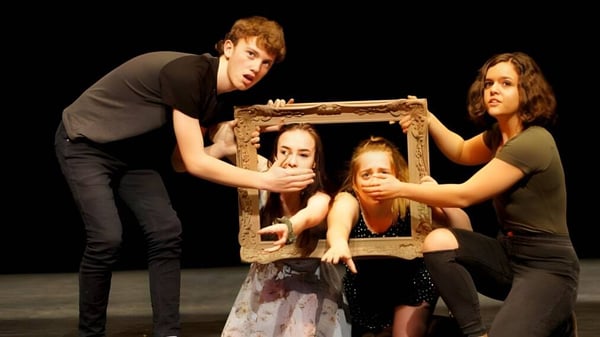 Cuatro estudiantes de la Bayridge Secondary School sostienen juntos un marco de madera frente a un fondo oscuro.