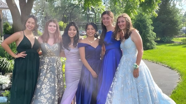 Cinco estudiantes de la Bayside Secondary School posan juntas en vestidos de colores en el área verde exterior de la escuela.