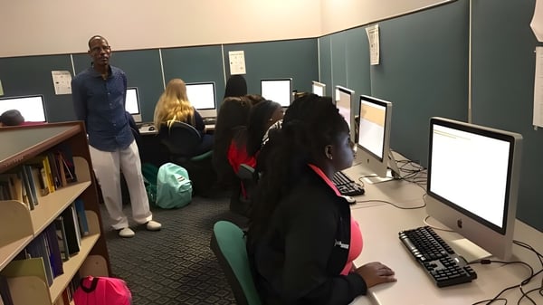 Estudiantes de la Beacon of Hope Christian School aprenden en computadoras en un aula con pizarra y estanterías.