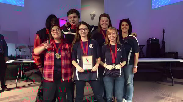 Un grupo de estudiantes de la Beacon of Hope Christian School está en el escenario con instrumentos musicales y tecnología de luces de fondo.