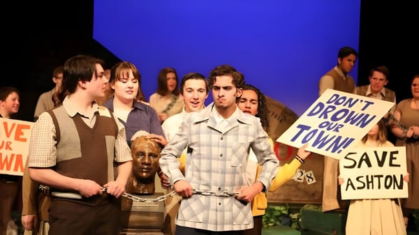 Estudiantes de la École Secondaire Beaumont Composite High School sostienen carteles y pancartas en una demostración frente a un fondo azul.