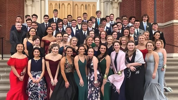 Un gran grupo de estudiantes de la Beckman Catholic School se reúne en ropa formal en las escaleras de un edificio histórico.