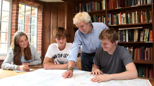 Un grupo de estudiantes y un hombre mayor trabajan juntos en una tarea en una sala llena de libros de la Bedales School.