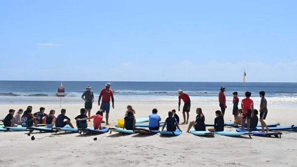 Estudiantes de la Bedford School están con sus tablas de surf en la playa frente al océano.